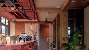 A wooden reception desk with a coffee machine, a plant, and a door in the background. - The Pink Boutique Hotel (Dalat)
