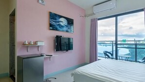 A hotel room with a bed, a TV, a painting, a desk, and a balcony with a view. - Dolphin B&B (Pingtung)