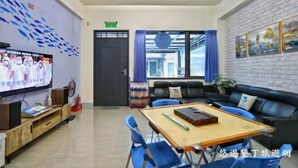 A modern room with a flat-screen TV, a wooden table, blue chairs, a black leather sofa, and a brick wall with framed pictures. - Dolphin B&B (Pingtung)