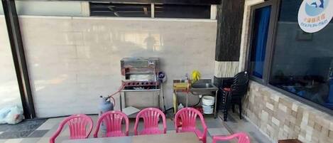 Une terrasse extérieure avec une table et des chaises, un barbecue et une fenêtre ornée d’un logo.