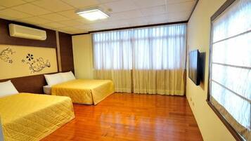 A hotel room with two beds, a television, and a large window with curtains.