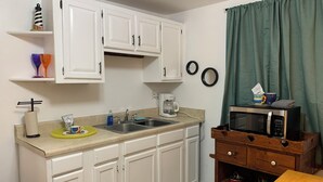 A compact kitchen with white cabinets, a sink, a coffee maker, a microwave, and a wooden storage unit. - Beach Side Studio #2 - Pet Friendly, WiFi, Off-Street Parking, Large Smart TV (Norfolk)