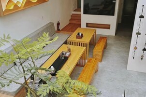 Una sala de estar con un sofá, una mesa de centro y un banco. Hay una planta en la esquina y un estante en la pared.