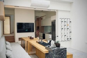 A modern living space with a sofa, a wooden dining table, a kitchen area, and a mounted TV.
