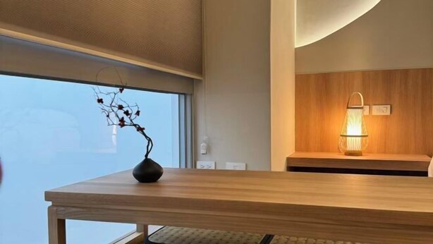 A modern interior with a wooden reception desk, a vase with branches, a wall-mounted lamp, and a large window. - Wuzheng Wood hall (Chiayi County)