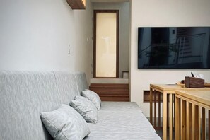 Una sala de estar moderna con un sofá gris, una mesa de comedor de madera y un televisor grande montado en la pared.