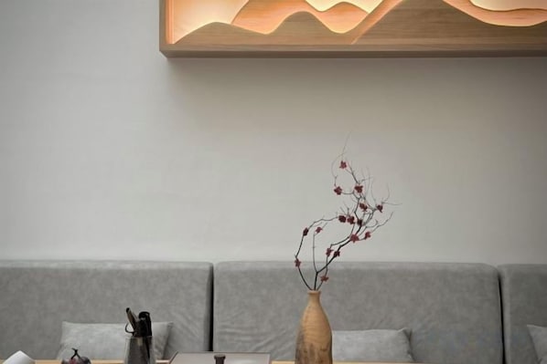 A modern interior with a grey sofa, a wooden vase with branches, and a wall-mounted light fixture.