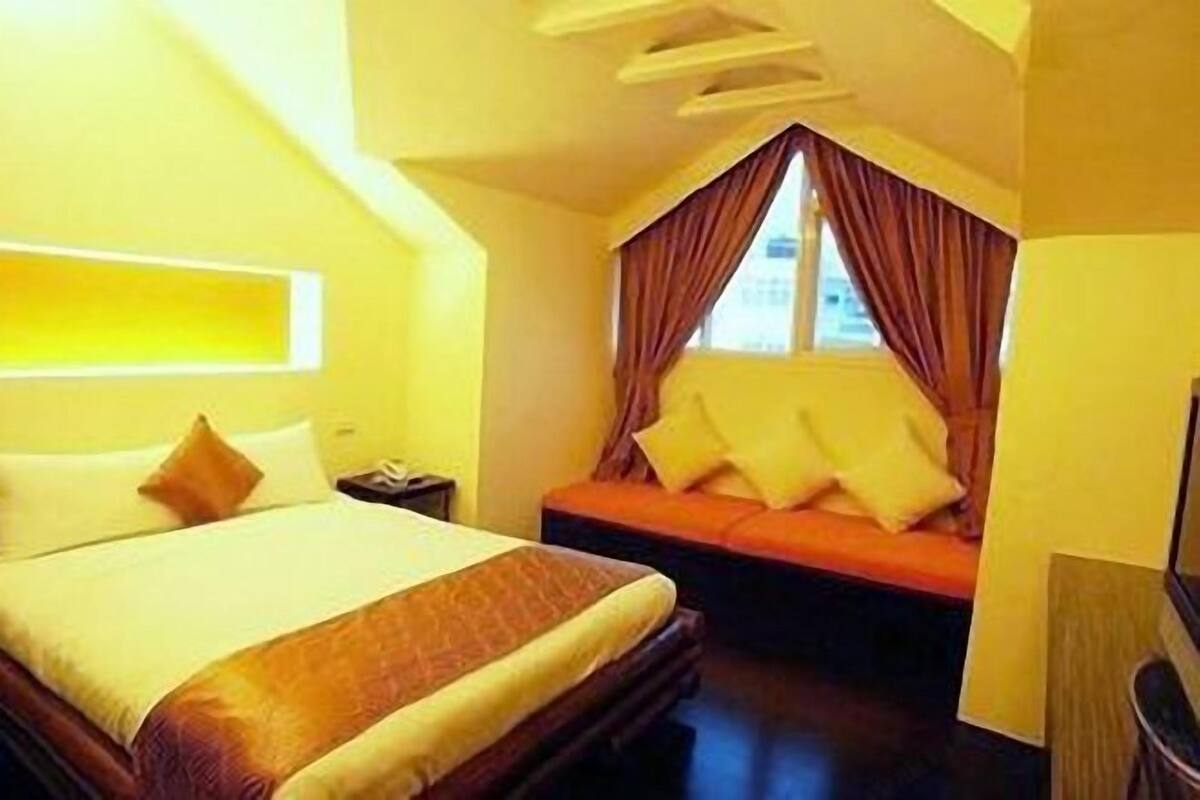 Una habitación de hotel con una cama, un sofá, una mesita de noche y una ventana con cortinas.