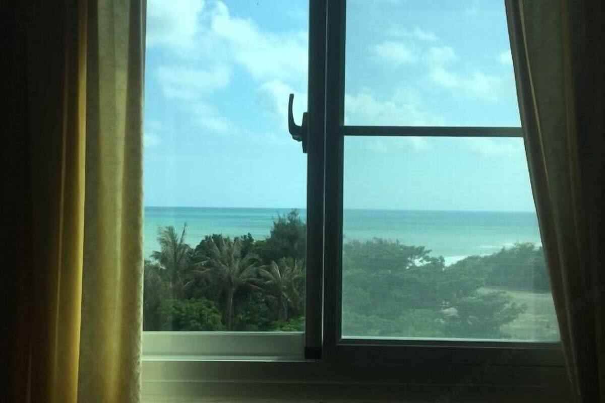 Una ventana con vista al océano y follaje.