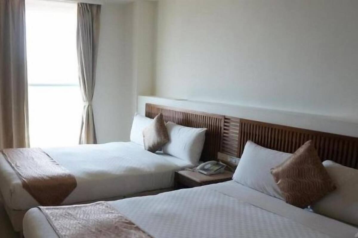 Habitación de hotel con dos camas, cabecero de madera, mesita de noche con teléfono y ventana con cortinas.