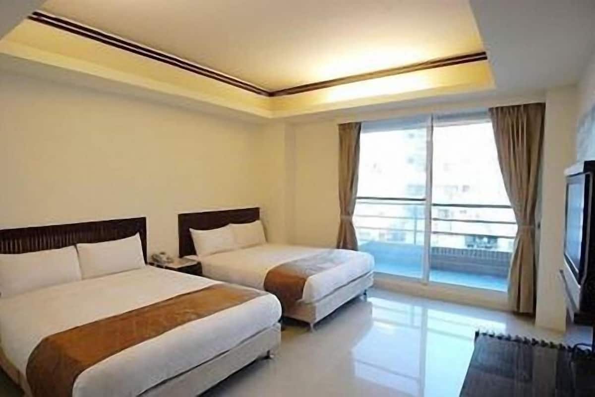 Una habitación de hotel con dos camas, un ventanal con cortinas y un televisor de pantalla plana.