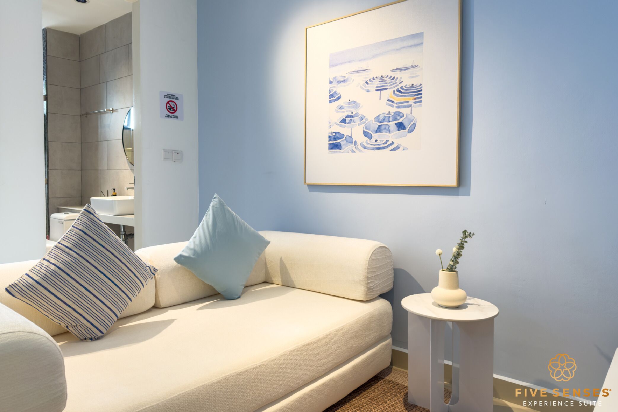 A modern bedroom with a beige sofa, a small side table with a vase, and a framed artwork on the wall.