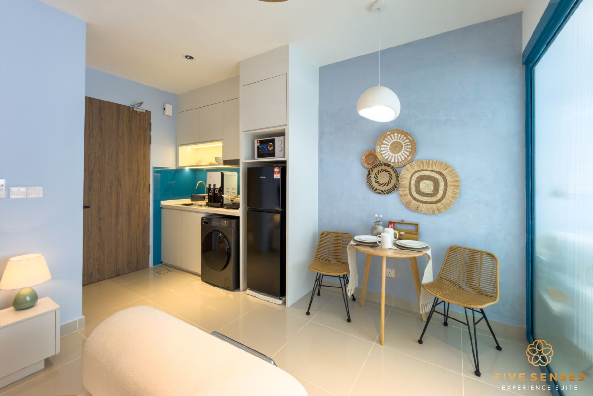 Una cocina moderna con cafetera, microondas y refrigerador. Hay un comedor con mesa y sillas, y una pared decorada con arte de pared tejido.