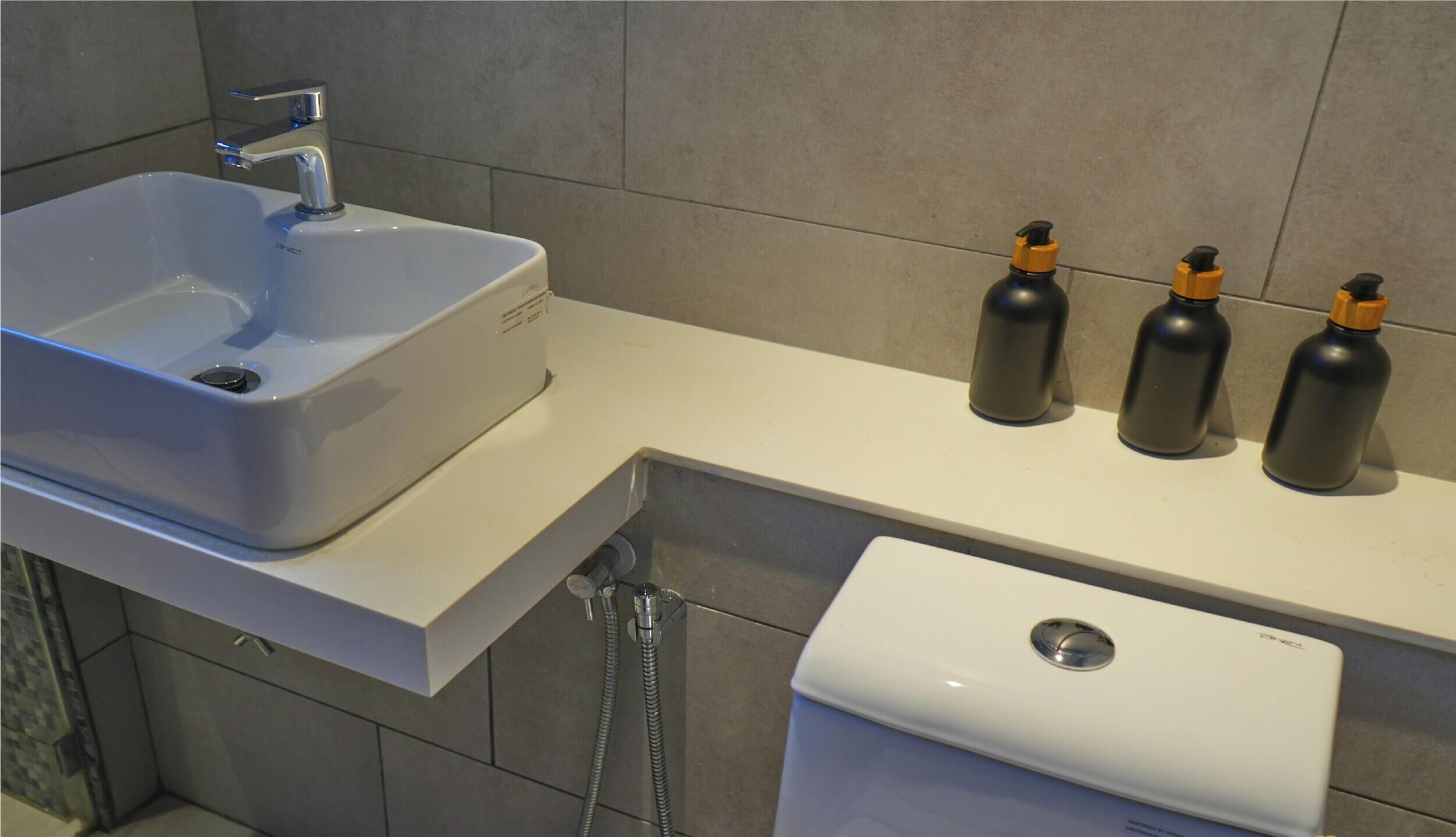 Een badkamer met een wit wastafel, toilet en drie zwarte flessen met gele dopjes op het aanrecht.