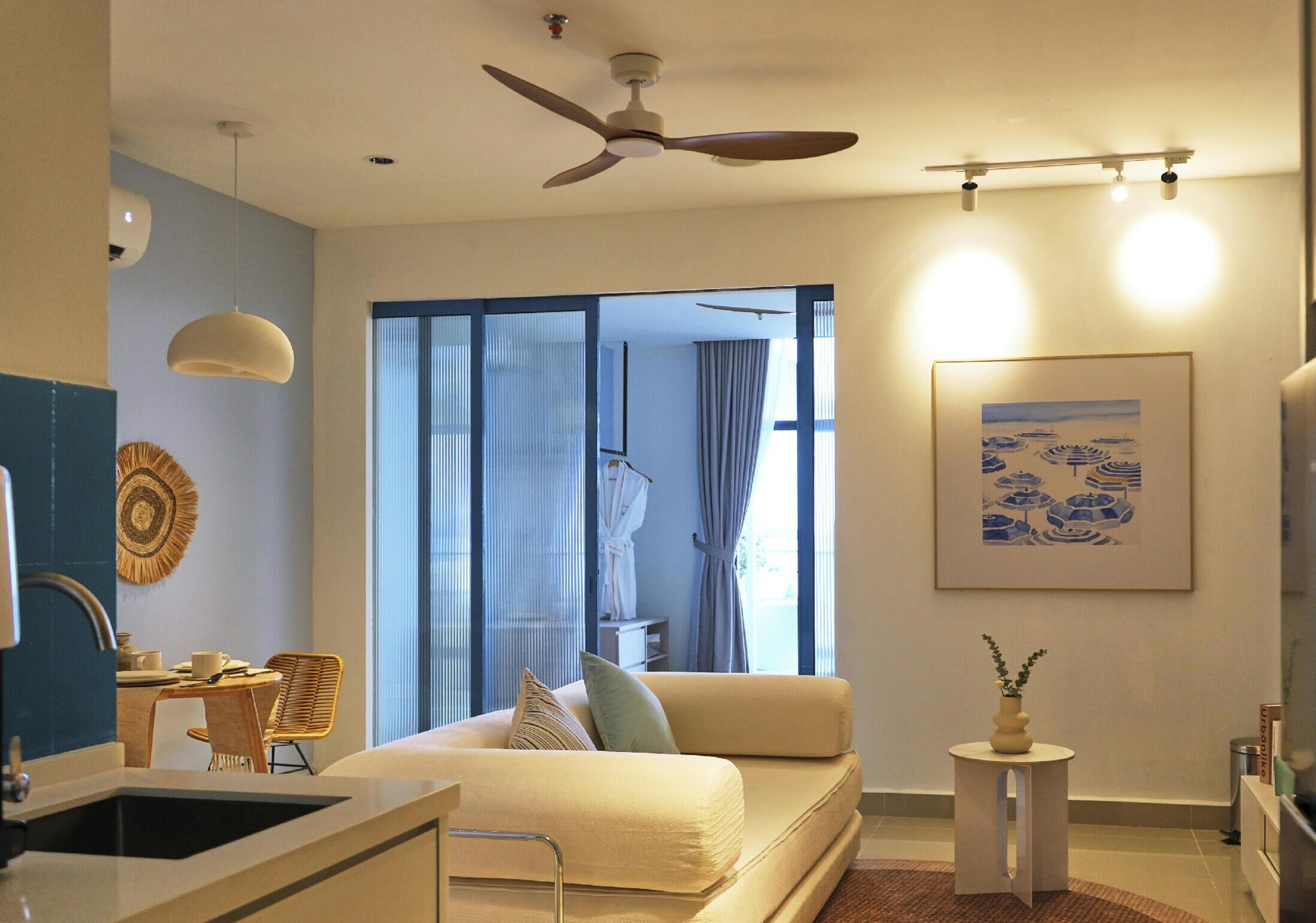 Una sala de estar moderna con un sofá, una zona de comedor con una mesa y sillas, un ventilador de techo y un ventanal con cortinas.