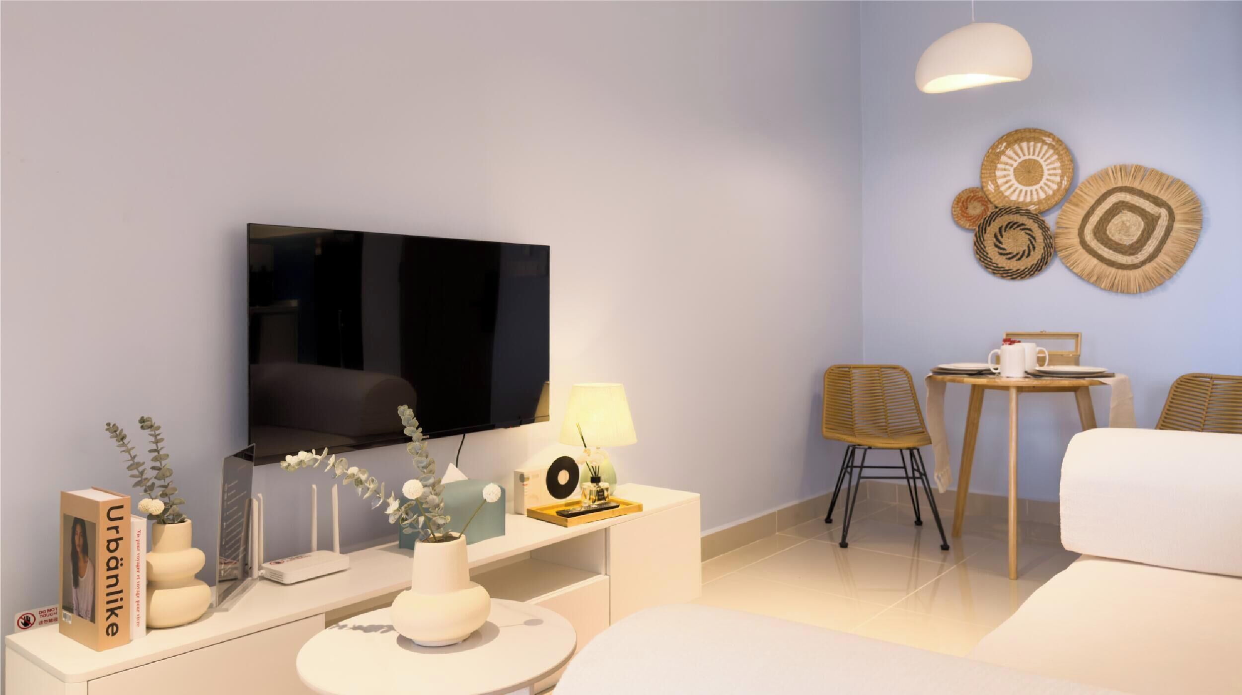 A modern living room with a flat-screen TV, a white sofa, a small round table, and two chairs.