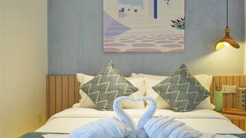 A hotel room with a bed, two patterned pillows, a wall-mounted painting, and a hanging light fixture.