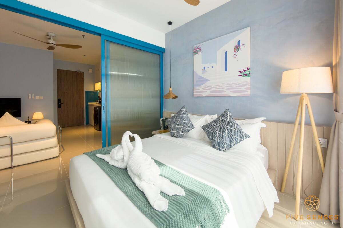 A modern hotel room with a bed, a green throw blanket, and a painting on the wall.