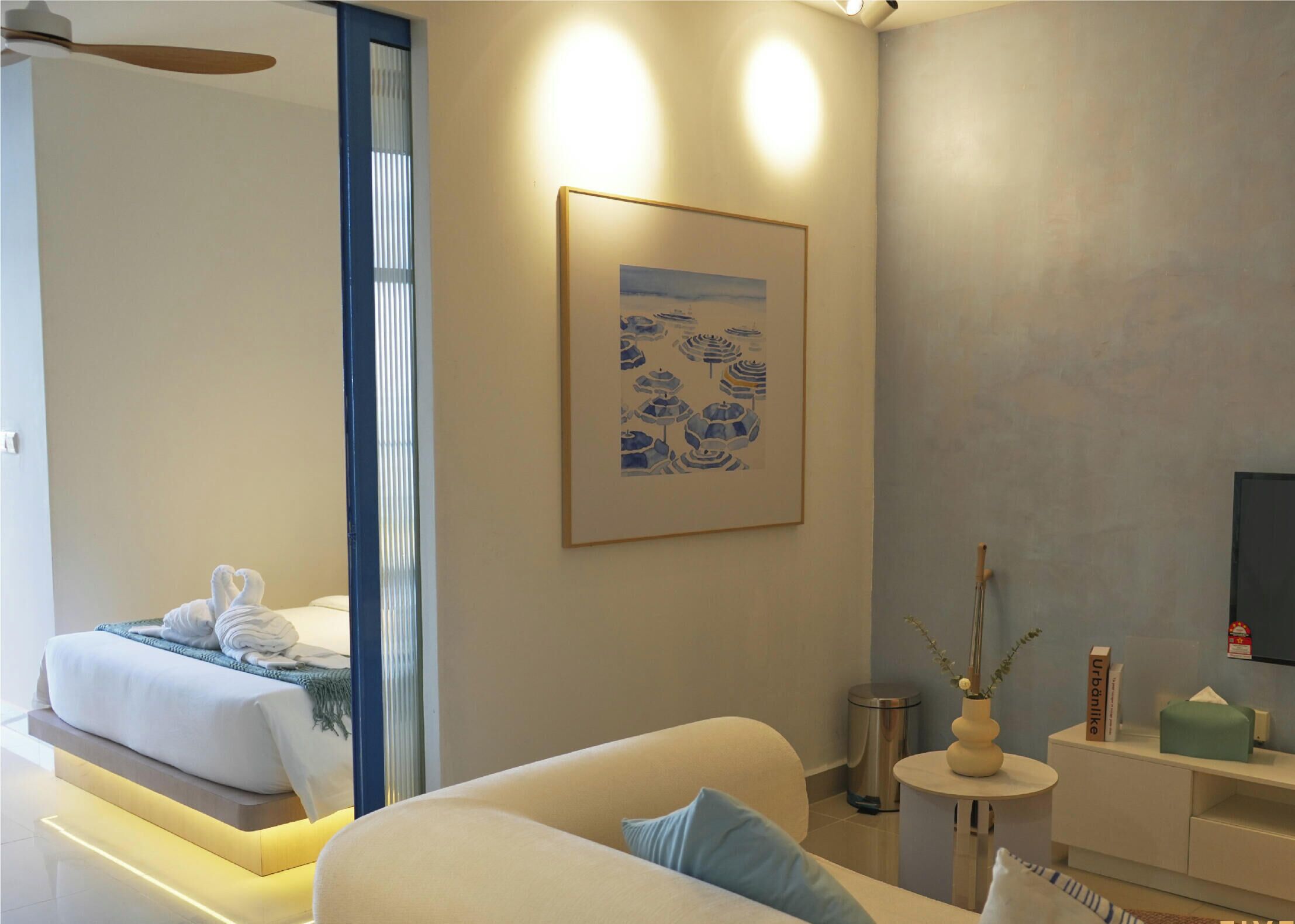 A modern hotel room with a bed, a sofa, a small table, and a painting on the wall.