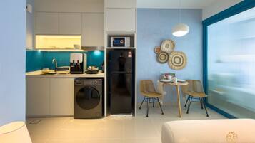 A modern kitchen with a dishwasher, washing machine, and a coffee machine. There is a dining area with two chairs and a table. The room has a large window and decorative wall art.