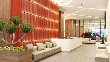 Una hall d'albergo moderna con reception, area salotto e un'ampia finestra che offre vista sull'interno.