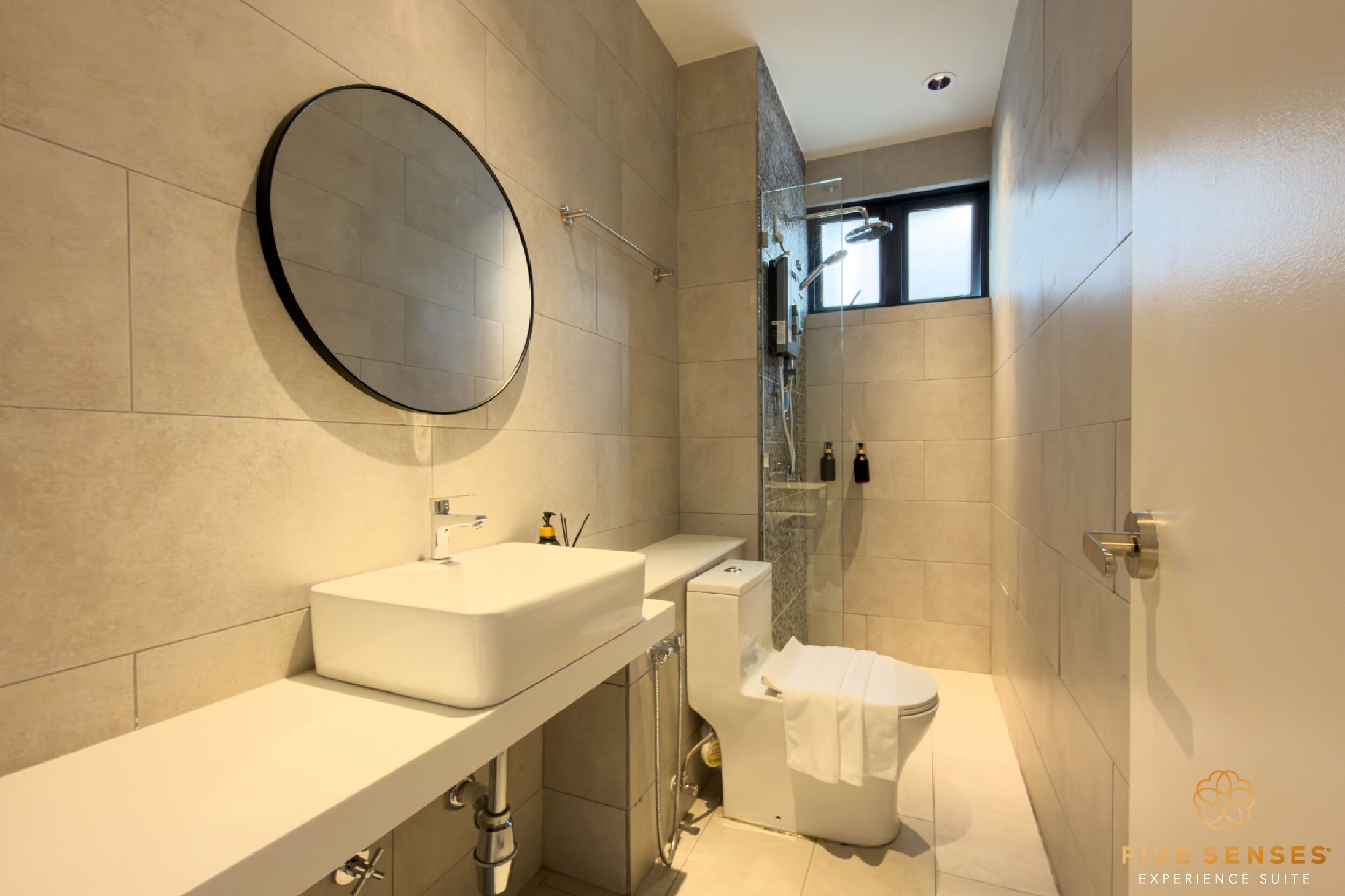 Un baño moderno con un espejo redondo grande, un lavabo blanco y una ducha con mampara de vidrio.