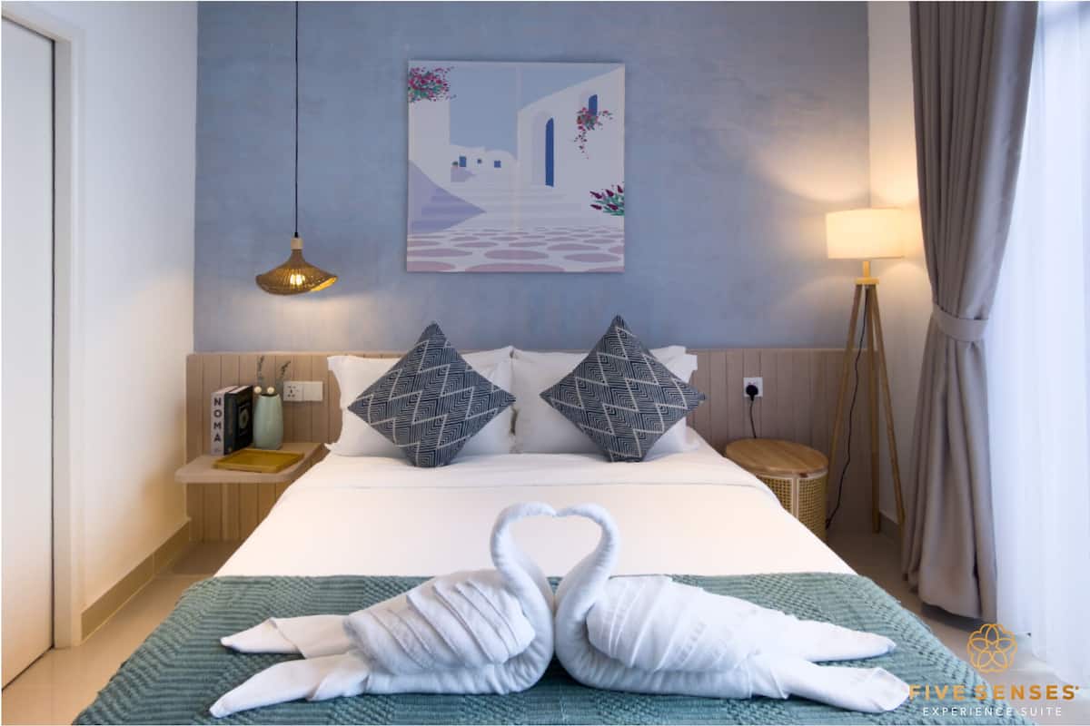 A hotel room with a bed, a wall-mounted artwork, a bedside lamp, and a decorative swan towel arrangement.