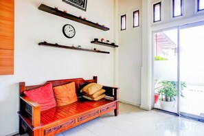 Ein Holzsofa mit Kissen, eine Wanduhr und Regale mit Dekorationselementen.