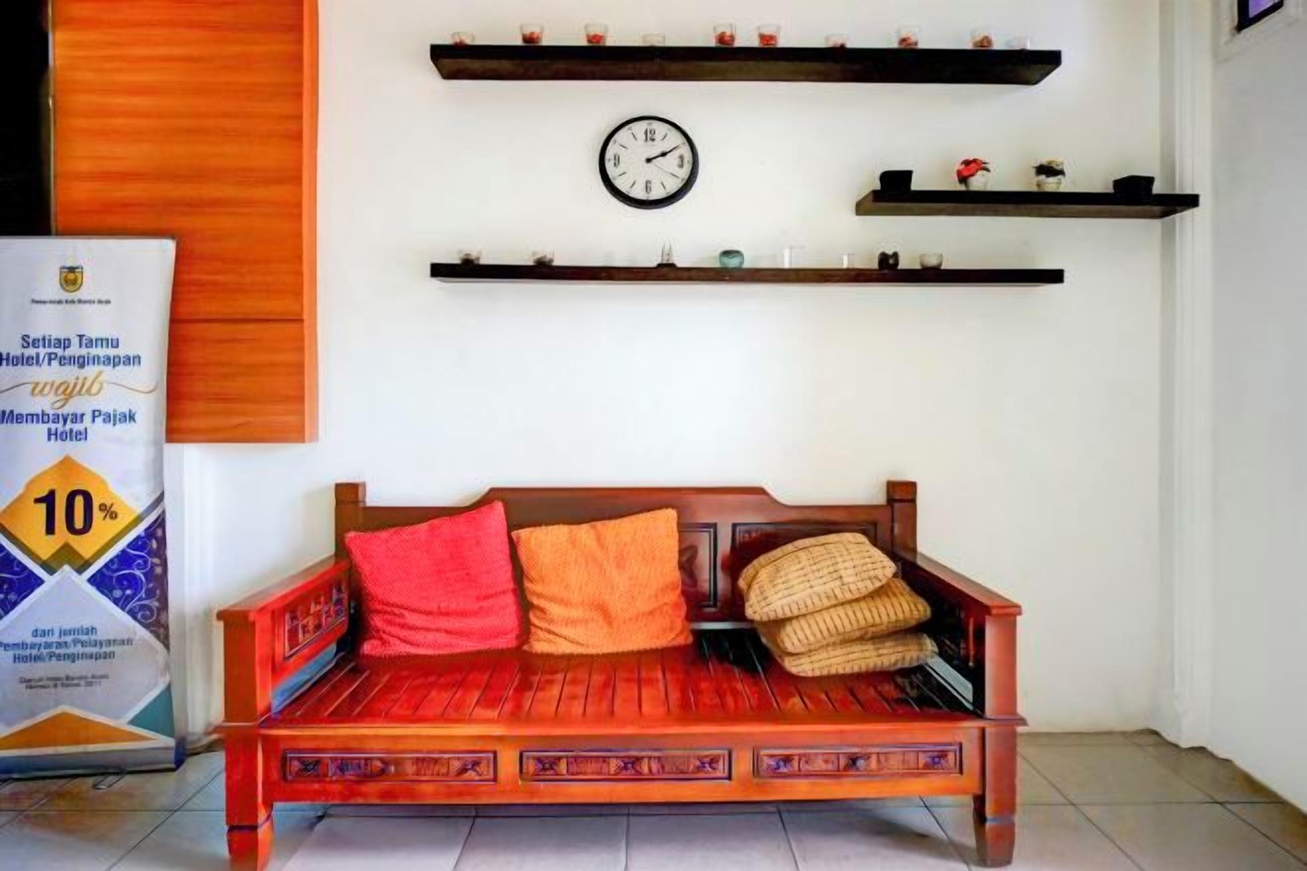 A traditional wooden sofa with cushions, a wall clock, and shelves with decorative items.