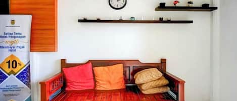 A traditional wooden sofa with cushions, a wall clock, and shelves with decorative items.