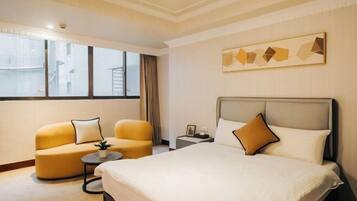 A hotel room with a bed, two armchairs, a small table, a nightstand, and a window with curtains.