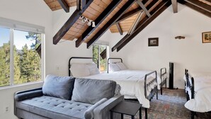 A bedroom with two beds, a sofa, and a view of trees through large windows. - Round Rock Lodge at Big Bear | Boulder Bay Modern Retreat w/ Pool Table | Minutes to Activities (Big Bear Lake)