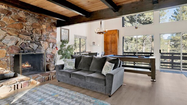 A cozy living room with a stone fireplace, a gray sofa, and a pool table. - Round Rock Lodge at Big Bear | Boulder Bay Modern Retreat w/ Pool Table | Minutes to Activities (Big Bear Lake)