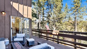 A deck with wicker furniture, a glass wall, and an American flag. - Round Rock Lodge at Big Bear | Boulder Bay Modern Retreat w/ Pool Table | Minutes to Activities (Big Bear Lake)