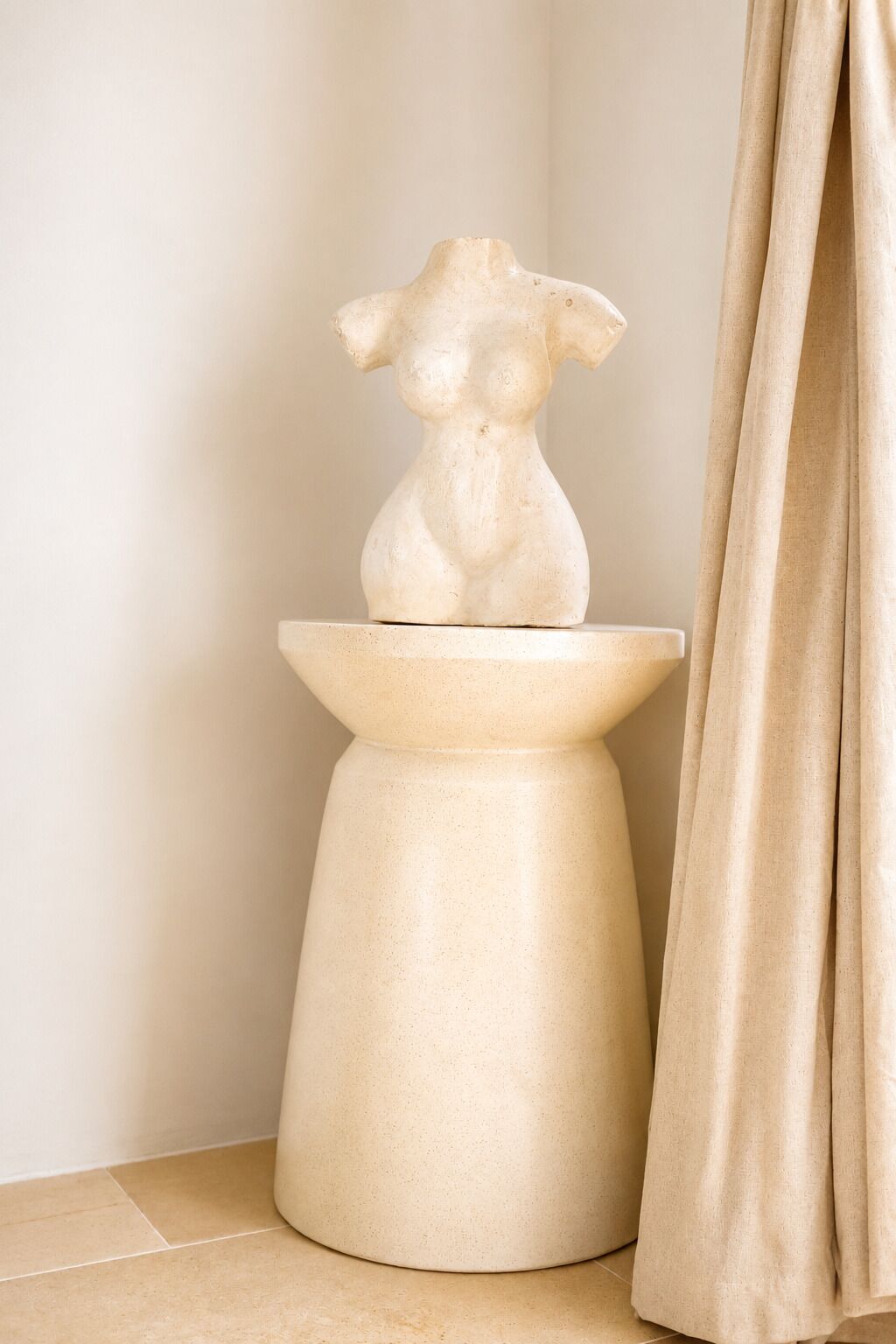 A sculpture on a pedestal in a corner with a curtain partially drawn.