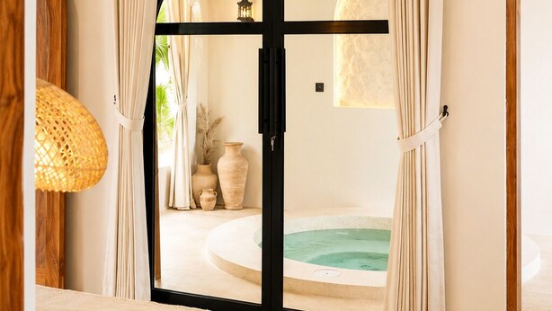 A bedroom with a bed, a ceiling fan, a view of a spa area through a doorway. - Okeanos Boutique Hotel Ungasan Uluwatu (Ungasan)