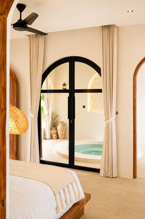 Une chambre avec un lit, un ventilateur de plafond et une vue sur un espace de spa, visible à travers une porte.