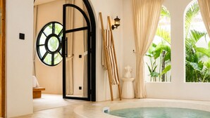 Ein Wellnessbereich mit einem runden Whirlpool, einer Holzschaukel und einem großen Fenster mit Vorhängen.