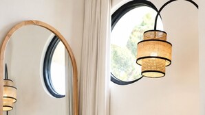 A room with a round mirror, a white chair, a woven basket with a teapot, and a hanging light fixture. - Okeanos Boutique Hotel Ungasan Uluwatu (Ungasan)