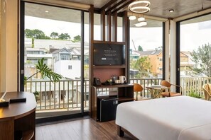 Une chambre d’hôtel avec un lit, un téléviseur fixé au mur, une petite table et un balcon donnant sur le quartier.