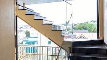 Una escalera con barandillas de vidrio que lleva a un balcón con vistas a edificios.