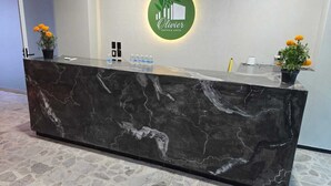 A reception desk with a marble top, a logo above it, and two potted plants on either side. - Your perfect stay awaits you in the heart of Uruapan! Olivier Suites & Lofts (Uruapan)