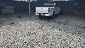A white pickup truck parked in a gravel driveway under a covered area with a metal roof. - Your perfect stay awaits you in the heart of Uruapan! Olivier Suites & Lofts (Uruapan)