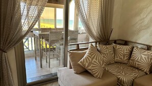 Ein modernes Wohnzimmer mit einer Couch, gemusterten Kissen und Blick auf einen Balkon mit Sitzgelegenheit.