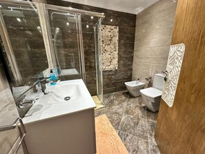 A modern bathroom with a glass-enclosed shower, a white sink, a bidet, and a toilet. - Luxury apartment by the sea (Martil)