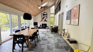 Amplia sala de estar con techo de madera, ventanas grandes, chimenea y piso de baldosas de piedra.