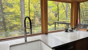 Una cocina con un ventanal que da a un bosque.