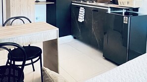 Una cocina compacta de diseño moderno, con encimera negra, estufa integrada y un lavamanos pequeño. Cuenta con un comedor con mesa y sillas de madera, y una despensa con refrigerador negro.