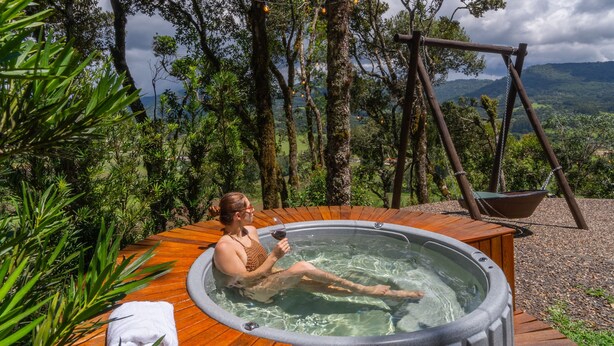 A hot tub with a wooden deck, surrounded by trees and a swing set. - Recanto do Bicí (Urubici)