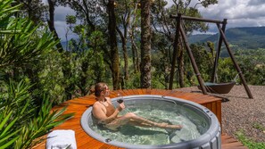 A hot tub with a wooden deck, surrounded by trees and a swing set. - Recanto do Bicí (Urubici)